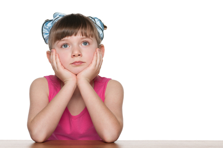 A pensive little girl sits at a school desk against the white の写真素材