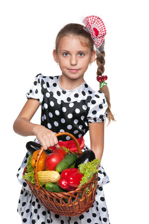 A smiling young girl holds a basket with vegetables on the white の写真素材