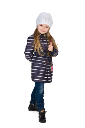A little girl in a striped coat holds her thumb up on the white backgroundの写真素材