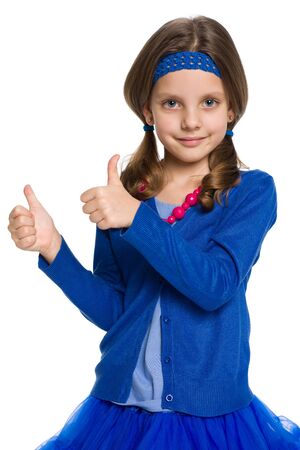 A pretty little girl with her thumbs up stands against the white backgroundの写真素材