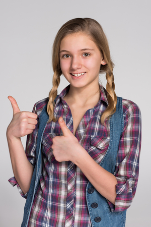 A pretty teen girl holds her thumbs up against the gray backgroundの写真素材