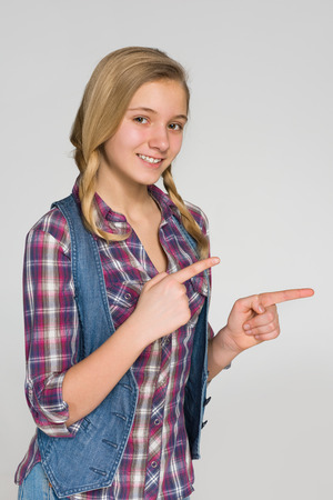 A blonde girl shows her fingers to the side against the white backgroundの写真素材