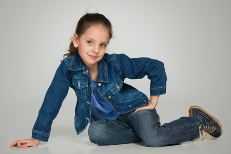 A happy little girl sits on the gray backgroundの写真素材