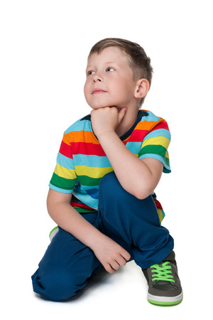A pensive blond little boy is sitting on the white backgroundの写真素材