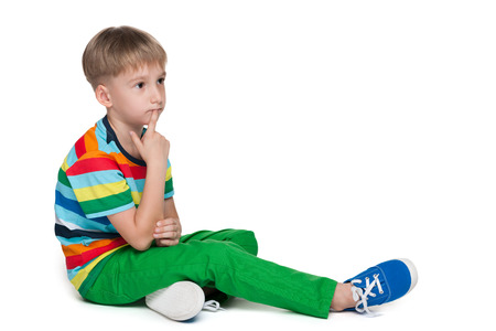 A thoughtful clever little boy is sitting on the white backgroundの写真素材