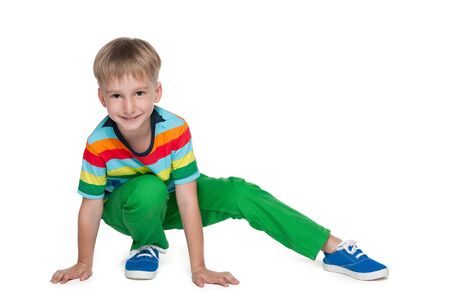 A little blond boy in a striped shirt is sitting on the white backgroundの写真素材