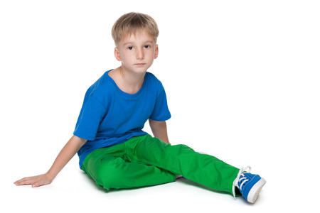 A serious little boy in a blue shirt is sitting on the white backgroundの写真素材