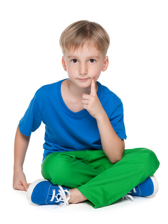 A thoughtful cute little boy is sitting on the white backgroundの写真素材