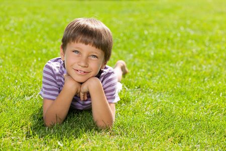 A happy little boy is lying on the green grassの写真素材