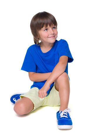 A smiling little boy in the blue shirt is sitting on the white backgroundの写真素材