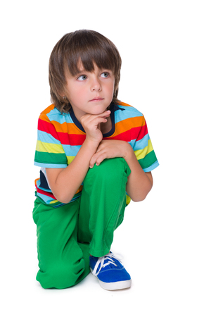 A pensive young boy in the green pants is sitting on the white backgroundの写真素材