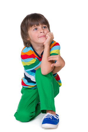 A smiling young boy in the green pants is sitting on the white backgroundの写真素材