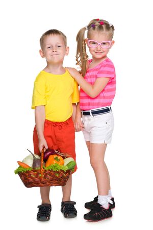 Two smiling children hold a basket of vegetablesの写真素材