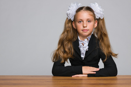 A schoolgirl sits at the desk against the gray backgroundの写真素材