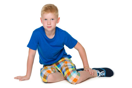 An upset boy in the blue shirt is sitting on the white backgroundの写真素材