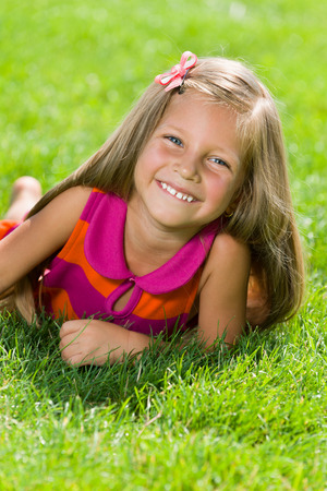 A happy little girl is lying on the green grass in a summer dayの写真素材