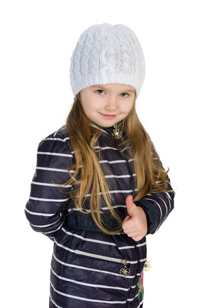 A little girl in a winter coat holds her thumb up on the white backgroundの写真素材