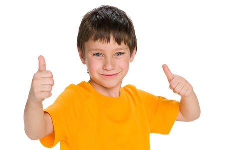 A smiling little boy in the yellow shirt holds his thumbs up on the white backgroundの写真素材