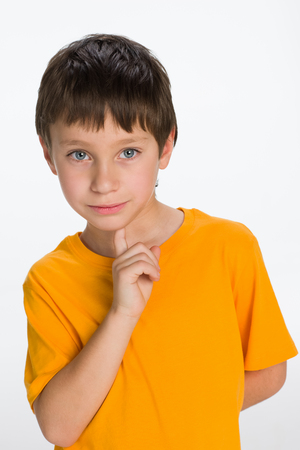 A thoughtful little boy in a yellow shirt stands on the white backgroundの写真素材