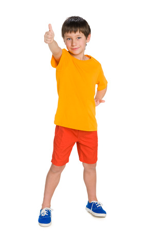 A cute young boy in the yellow shirt with his thumb up stands against the white backgroundの写真素材