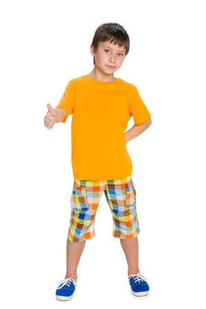 A cute little boy in the yellow shirt with his thumb up stands against the white backgroundの写真素材