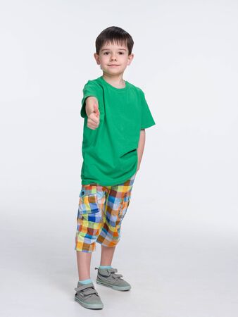 A cute young boy in a green shirt with his thumb up standsの写真素材