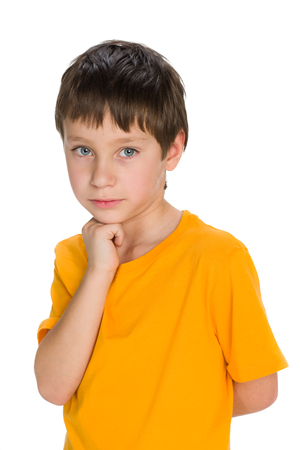 A thoughtful young boy in a yellow shirt stands on the white backgroundの写真素材