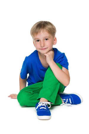 A blond little boy in the green pants sits on the white backgroundの写真素材