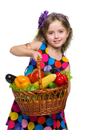A smiling little girl with a basket of vegetables on the white backgroundの写真素材