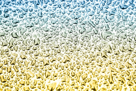 Water drops on metal background with reflection blurred on the edges. Image processing with blue and yellow colors and gradient filter effectsの写真素材