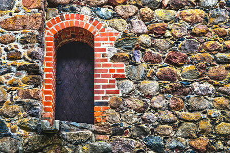 Old steel door framed red bricks in stone wallのeditorial素材