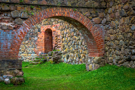 Stone arch and wall in internal courtyard of castle with green grass and doorwayのeditorial素材