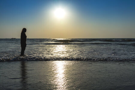 Scenic view from beach in Goa to beautiful sunrise above the Arabian sea. Silhouette of woman or girl looks at seaの写真素材