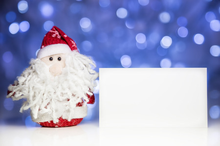Santa Claus or Father Frost with greeting white blank card on Christmas lights background on white surfaceの写真素材
