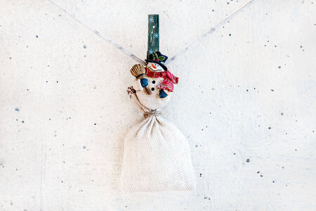 Christmas snowman clothespin hanging at center on clothesline or rope and holding sack on white plaster backgroundの写真素材