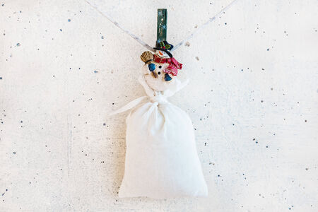 Christmas snowman clothespin hanging at center on clothesline or rope and holding big sack on white plaster backgroundの写真素材