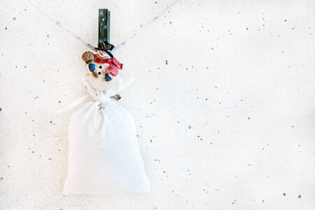 Christmas snowman clothespin hanging at left on clothesline or rope and holding big sack on white plaster backgroundの写真素材