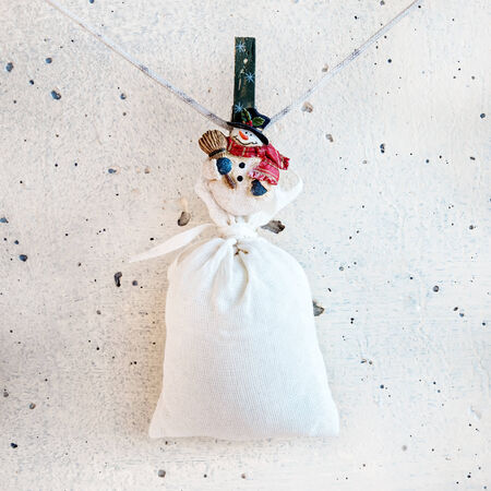 Christmas snowman clothespin hanging on clothesline or rope and holding big sack on white plaster backgroundの写真素材