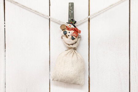 Christmas snowman clothespin hanging at center on clothesline or rope and holding big sack on white wood backgroundの写真素材