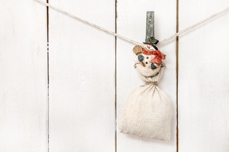 Christmas snowman clothespin hanging at right on clothesline or rope and holding big sack on white wood backgroundの写真素材