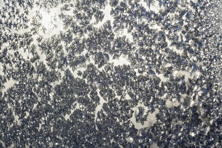 Ice snowflakes and frost pattern over the sun on frozen Christmas winter window. Colored in gray or silver tone. Selective focus at center with blur edges of imageの写真素材