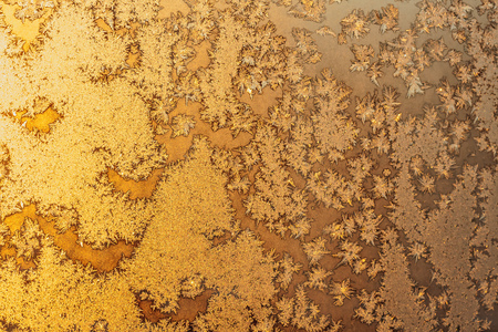 Ice snowflakes and frost pattern on frozen Christmas winter window. Colored in yellow or gold tone. Selective focus at center with blur edges of imageの写真素材