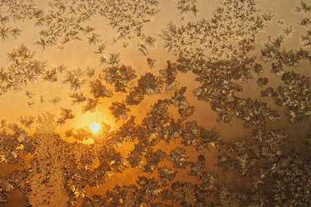 Ice snowflakes and frost pattern over the sun on frozen Christmas winter window. Colored in yellow or gold tone. Selective focus at center with blur edges of imageの写真素材