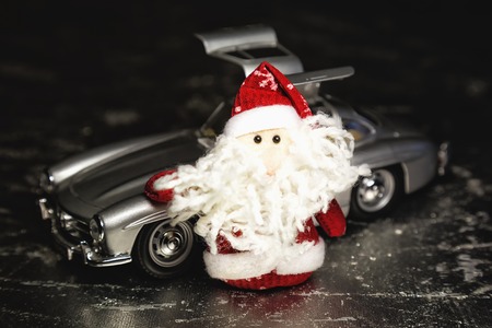 Santa Claus or Father Frost with old vintage automobile on on silver or metal grunge surface. Main focus of image on Santa Claus and selective on turned left and opened doors toy retro carの写真素材