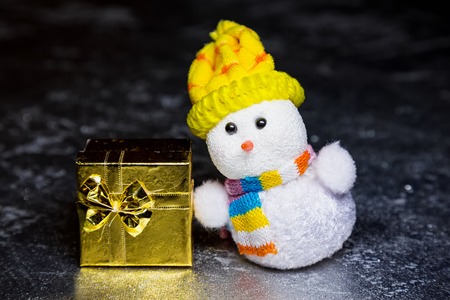 Christmas snowman toy and gold or yellow gift box or present on silver or metal grunge surfaceの写真素材