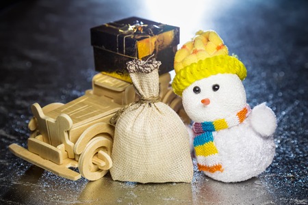 Christmas snowman toy and old vintage wooden automobile with golden or yellow gift box and sack on silver or metal grunge surface with backlight from behind. Main focus of image on Santa Claus and selective wood carの写真素材