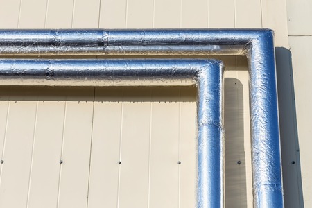 Metal chrome pipes on yellow plastic siding wallの写真素材