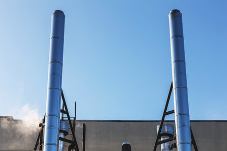 Smoke metal pipes on rooftop of industrial building against blue sky backgroundの写真素材