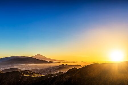 Sun with sunlight over mountains on blue sky with haze and Teide volcano on background at evening sunset in Tenerife Canary island, Spain at spring or summerの写真素材