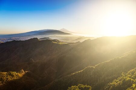 Sun with sunlight over mountains on blue sky with fog or haze and Teide volcano on background at evening sunset in Tenerife Canary island, Spain at spring or summerの写真素材